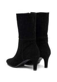 Un par de botas de ante negro hasta la mitad de la pantorrilla con punta redonda y tacones altos y delgados, mostradas desde un ángulo trasero en un fondo blanco.