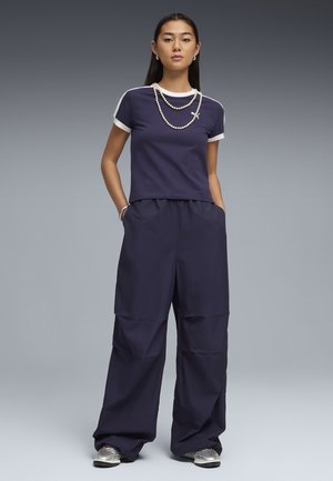 T-shirt à col rond bleu marine avec accents blancs, associé à un pantalon ample bleu marine ; comprend des poches et des baskets grises avec un motif texturé.