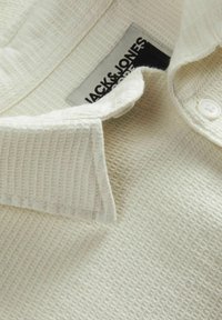 Weißes, strukturiertes Poloshirt mit kleinem Kragen und zwei Knopfverschluss. Verfügt über ein sichtbares Markenetikett in Schwarz und Grau.