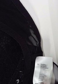 Tissu de soutien-gorge en dentelle noire avec motif floral et détails en maille, montrant une étiquette blanche de composition du tissu avec pourcentage d'élasthanne.