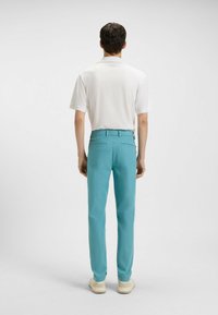 Biała koszulka polo z krótkim rękawem, zestawiona z turkusowymi zwężającymi się spodniami, z tylnymi kieszeniami i gładkim, lekkim materiałem.