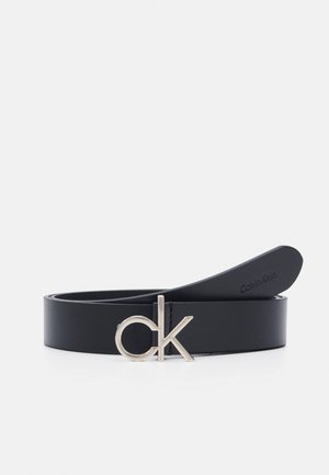 Zwarte leren riem met zilveren "ck" logo gesp en geperst "Calvin Klein" op het uiteinde, opgerold tegen een witte achtergrond.