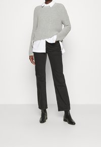 Szary prążkowany sweter z dzianiny nałożony na białą koszulę zapinaną na guziki, w zestawie z czarnymi spodniami o prostych nogawkach i czarnymi botkami za kostkę.