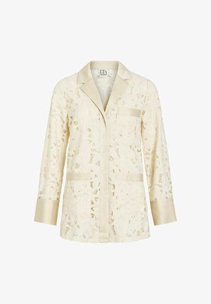 Kremowa bluzka z koronki z długim rękawem, z satynowym kołnierzem, mankietami, zapinana na guziki z przodu, posiadająca trzy kieszenie i kwiatowe wzory z wycięć.