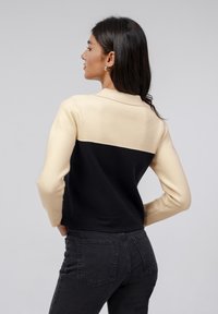 Zwart en crème kleurblokken trui met een kraag, lange mouwen en een aangesloten ontwerp. Gebreide textuur; gedragen met donkere jeans.