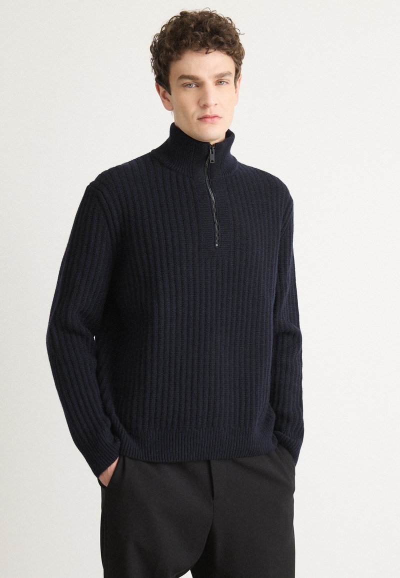 Sweater de malha canelada azul-marinho com colarinho alto e fecho de meio zíper. Mangas longas e corte descontraído, feito de tecido suave.