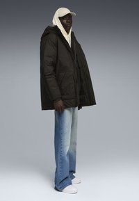 Sort pufferjakke med hætte, parret med en cremet hoodie, lyseblå jeans og hvide sneakers. Jakken har sidelommer.