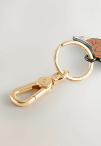 Guld metal nøglering med en rund ring og en klips, der har en vedhæftet charm i form af et farverigt blomsterdesign.