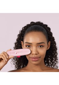 Un dispositif facial rose tenu contre la joue, présentant un design lisse et arrondi avec un accent Hello Kitty et des boutons de contrôle.