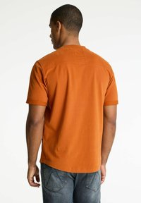 T-shirt arancione a maniche corte con una superficie in cotone morbido, dotato di scollo a girocollo e dettagli di cucitura sulle spalle.