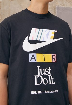 Personne portant un t-shirt noir Nike avec le texte multicolore "NIKE" et "AIR", le logo swoosh blanc et le slogan "Just Do It."