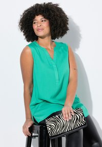 Una canotta senza maniche di colore turchese con un design a scollo a V è abbinata a una clutch a strisce zebrate in bianco e nero e a leggings neri lucidi.