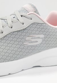 Zapatillas gris claro con parte superior de malla texturada, con un suave acento rosa alrededor del cuello y una suela blanca acolchada. Detalle del logo plateado.