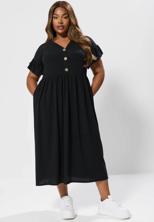 Czarna midi sukienka o prążkowanej teksturze, z krótkimi falbaniastymi rękawami, dekoltem w serek i trzema guzikami z przodu. Noszona z białymi trampkami.