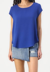 Top blu corto a maniche corte con scollatura rotonda, realizzato in tessuto liscio, abbinato a una gonna in denim strappata con bordi sfrangiati e design asimmetrico.