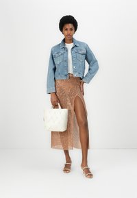 Džinsena jakna, bela majica, bleščeča rjava krila s visokim razporkom in tkana bela torbica. Sandali na odprti prsti dopolnjujejo videz.