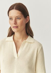 Polo shirt di maglia giallo chiaro con colletto aperto corto e maniche corte, caratterizzato da un motivo testurizzato su tutta la superficie.