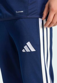 Pantalones deportivos Adidas de color azul marino con tres franjas blancas a lo largo de los lados, con una etiqueta "CLIMACOOL" y un pequeño logotipo triangular blanco.
