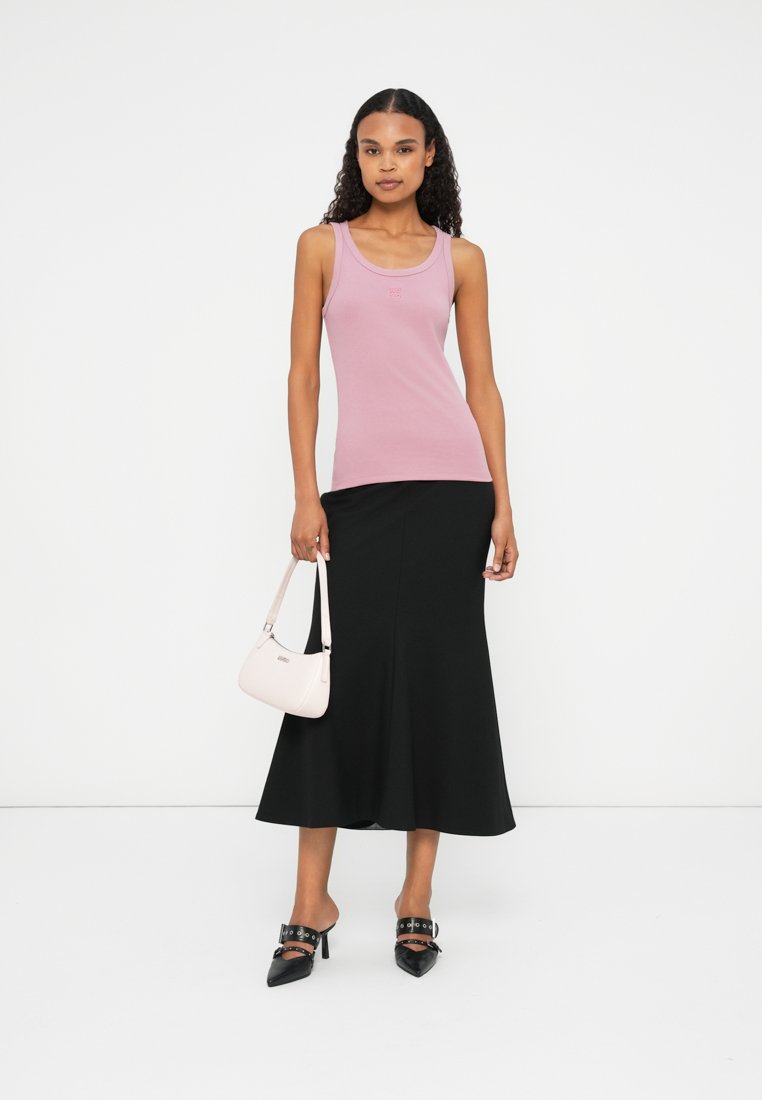 Haut sans manches rose clair associé à une jupe noire évasée. L'ensemble est complété par un petit sac à main rose et des chaussures à talons hauts noires.