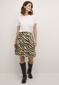 Jupe à rayures zèbre kaki avec une taille élastique, associée à un t-shirt blanc et des bottes noires jusqu'aux genoux. Texture lisse, design décontracté.