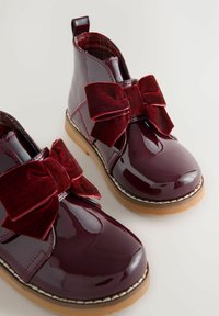 Burgunderfarbene patentierte Leder-Stiefeletten mit großen Samt-Schleifen, kontrastierenden gestickten Details und einer strukturierten Gummisohle.