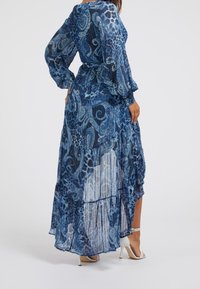 Robe maxi en bleu avec un imprimé cachemire et léopard, manches bouffantes longues, taille cintrée et ourlet à volants en étages. Tissu semi-transparent et fluide.