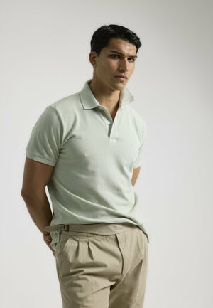 Camisa polo de algodón en verde menta claro con mangas cortas, con un cuello clásico y una discreta botonera, combinada con pantalones beiges.