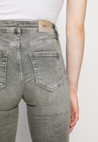 Grijs, high-waisted denim jeans met een leren label met "ONLY", twee achterzakken en een getailleerd ontwerp. Gladde textuur.