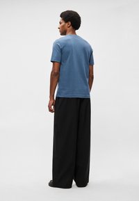 T-shirt de algodão azul com mangas curtas, decote redondo e corte descontraído, combinado com calças largas pretas. Textura lisa, sem padrões visíveis.