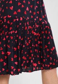 Robe plissée en tissu bleu marine avec un motif de cœurs rouges, alliant texture douce et design léger.