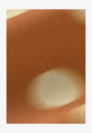 Tissu brun avec une tache circulaire beige clair ou blanche au centre, mettant en valeur la texture et le contraste des couleurs.