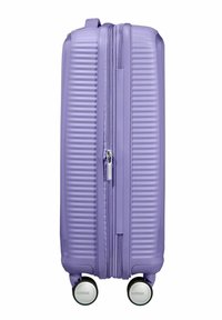 Valigia rigida viola con texture a coste, doppia cerniera e quattro ruote. Dotata di manico superiore per un facile sollevamento e trasporto.