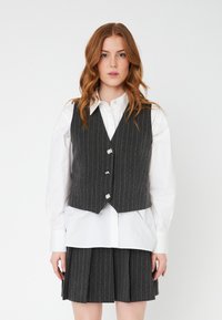 Gray pinstripe vest with silver buttons, layered over a white collared shirt, paired with a matching pleated gray skirt. Cotton blend material.