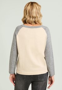 Jasnobeżowy sweter z szarymi raglanowymi rękawami, ściągaczami na mankietach i u dołu, miękka tekstura, prosty krój i minimalistyczny design. Odpowiedni do codziennego noszenia.