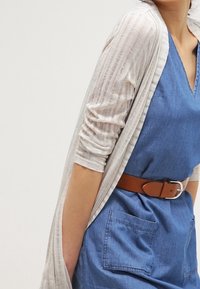 Lehounký, průsvitný cardigan s krémovými pruhy přes modro-denimové šaty, protažený širokým hnědým páskem. Má dlouhé rukávy a výstřih do V.