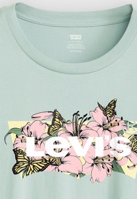 Light green t-shirt featuring a floral graphic in pink with butterflies, the brand name "Levi's" in bold white text, and a textured crew neck.