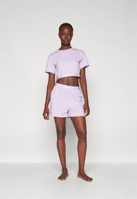 T-shirt cropped lavande clair et shorts assortis. Les deux en tissu doux avec le logo "HUGO" sur la ceinture et l'ourlet, coupe décontractée.