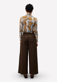 Langärmliges, enges Oberteil mit einem Design in braun, blau und weiß; kombiniert mit weiten, dunkelbraunen Hosen, die über Gesäßtaschen verfügen.