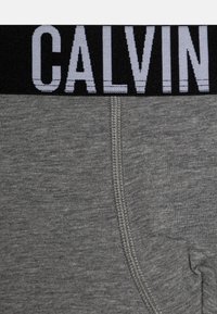 Grijze katoenen boxershorts in een gemengde stof met een zwarte elastische tailleband waarin "CALVIN" in lichtgrijs is geweven. Gladde textuur met een aansluitende pasvorm.