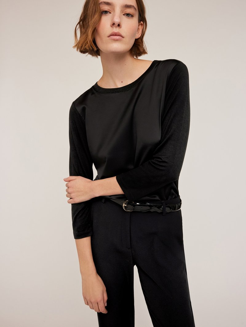 Czarna bluzka z rękawami trzyczwartowymi, gładką fakturą i okrągłym dekoltem. Noszona z czarnym paskiem z okrągłą klamrą i plecionym wzorem.