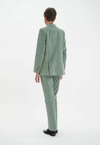 Un costume en velours côtelé vert clair comprenant une veste ajustée avec un col à cran et un pantalon assorti, affichant une texture lisse et des lignes épurées.