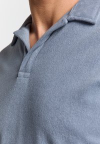 Lichtblauw poloshirt van een zachte, textuurrijke stof. Kenmerkt zich door een klassieke kraag en subtiele stikdetails bij de halslijn.