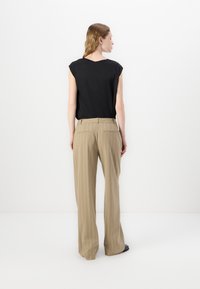 Black sleeveless top paired with beige pinstriped trousers. Trousers feature a tailored fit with front and back pockets, smooth texture.