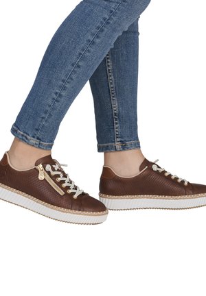 Brown leather sneakers with a textured design, white rubber sole, lace-up front, and a side zipper accent. Worn with blue jeans.
