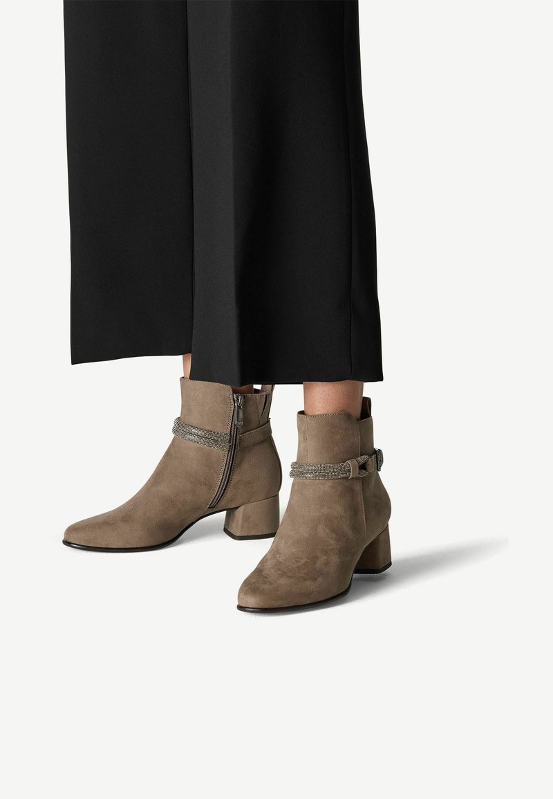 Bottines en daim taupe avec un talon bloc, fermeture éclair sur le côté et une sangle décorative avec des accents métalliques. Fini texturé.
