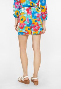 Rompers floreali colorati con una vita aderente e due tasche posteriori, caratterizzati da fiori blu, rosa, arancione e teal su uno sfondo chiaro.