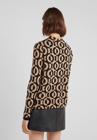 Sweter z dzianiny w kolorze tan i czarnym, z okrągłym wzorem, posiadający okrągły dekolt i długie rękawy. Szczegóły dotyczące akcesoriów są niewidoczne.