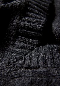 Svart stickad tyg som visar ribbad struktur och mjuk, fuzzy yta med varierande djup och mönster. Nära vy framhäver materialets detaljer.