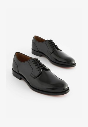 Musta nahkasandaalit kiillotetulla pinnalla, pyöreällä varpaalla ja nauhakiinnityksellä, joissa on matala korko ja sileä rakenne.