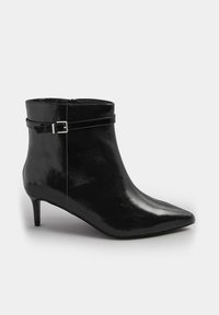 Botín de charol negro con punta afilada, tacón cónico y detalle de correa con hebilla alrededor del tobillo. Textura suave.